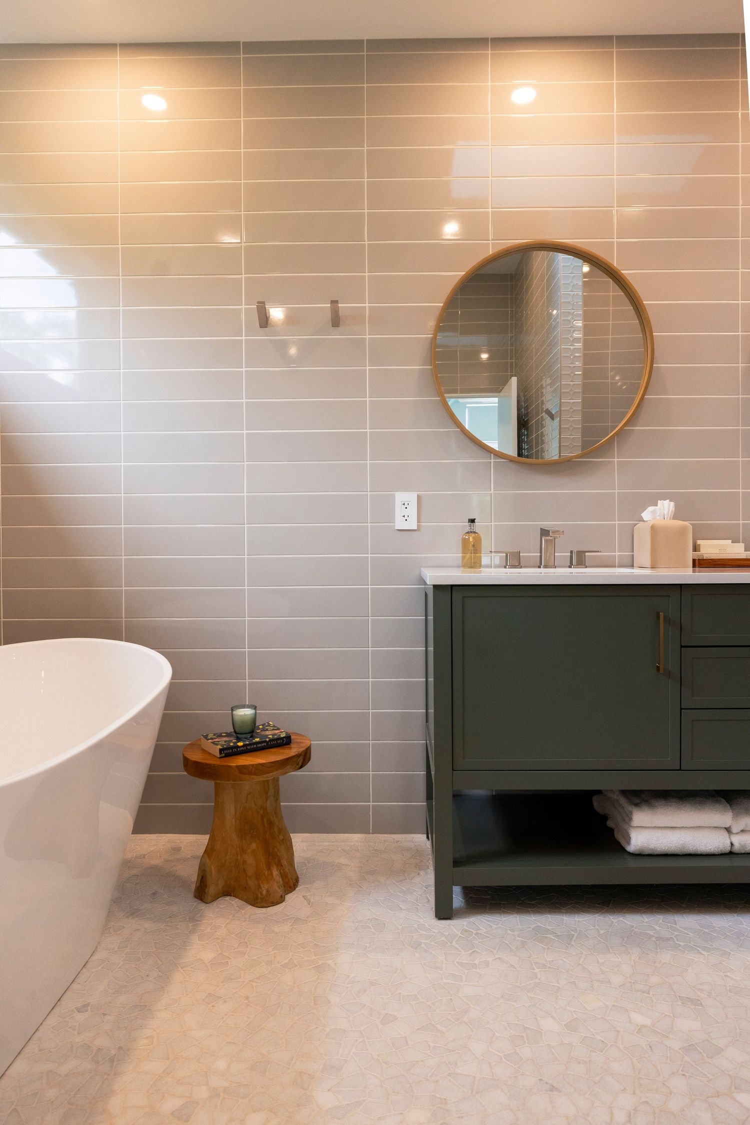 Modern bathroom interior with gray tile walls, round mirror, and dark green vanity cabinet.