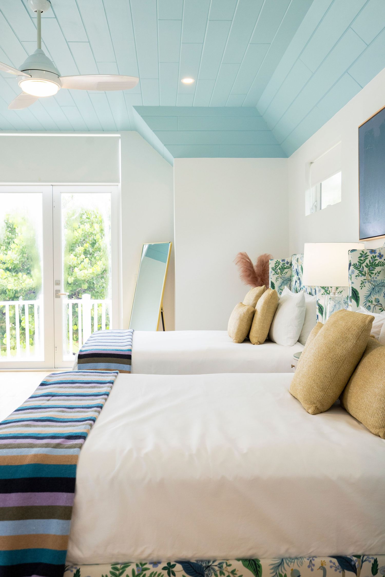 Bright coastal bedroom with turquoise ceiling, white bedding, and striped accent pillows.