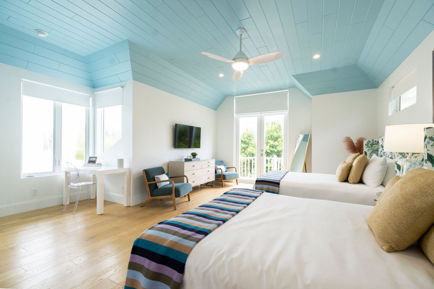 A blue-painted bedroom ceiling creates a bright, airy atmosphere with light wood floors and coastal decor.