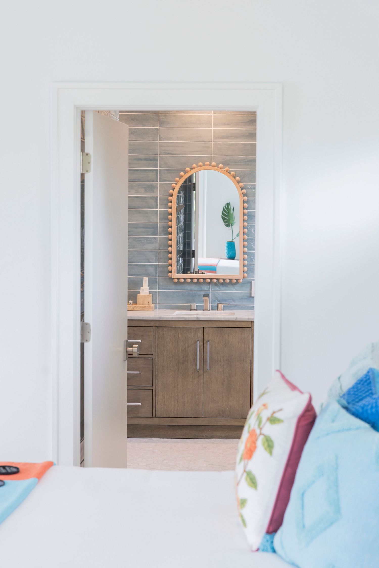 Contemporary bathroom with grey tile backsplash, wooden vanity, and arched mirror design.