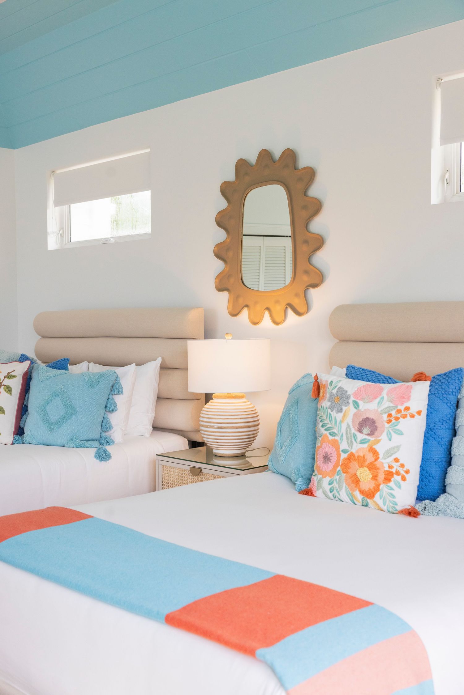 Coastal-themed bedroom with turquoise ceiling, decorative sun mirrors, and coral accent pillows.