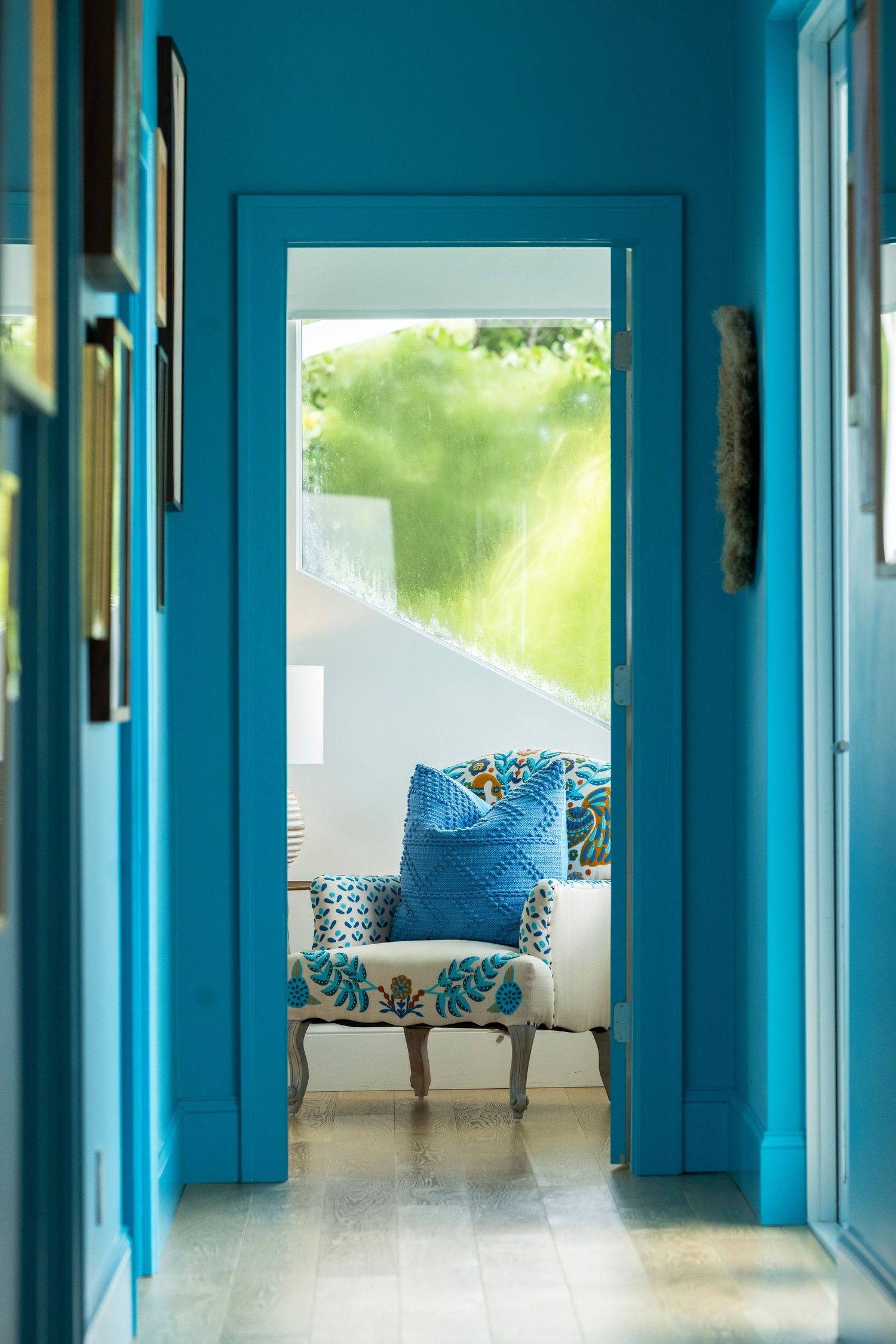 Long hallway painted in vibrant turquoise blue with white trim and natural lighting.