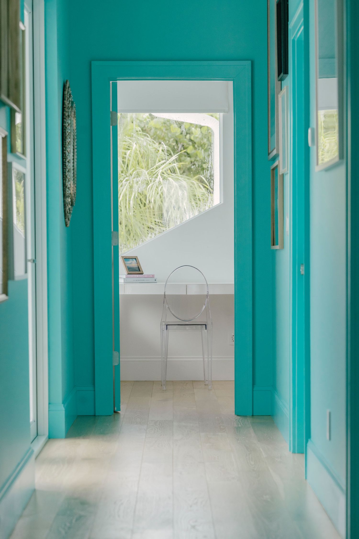 Modern hallway featuring turquoise walls, white trim, and large windows letting in natural light.
