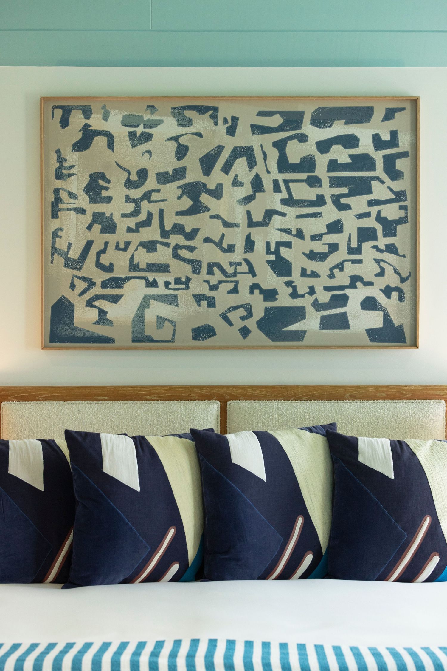 Contemporary bedroom wall art featuring abstract blue patterns above geometric navy and white throw pillows.