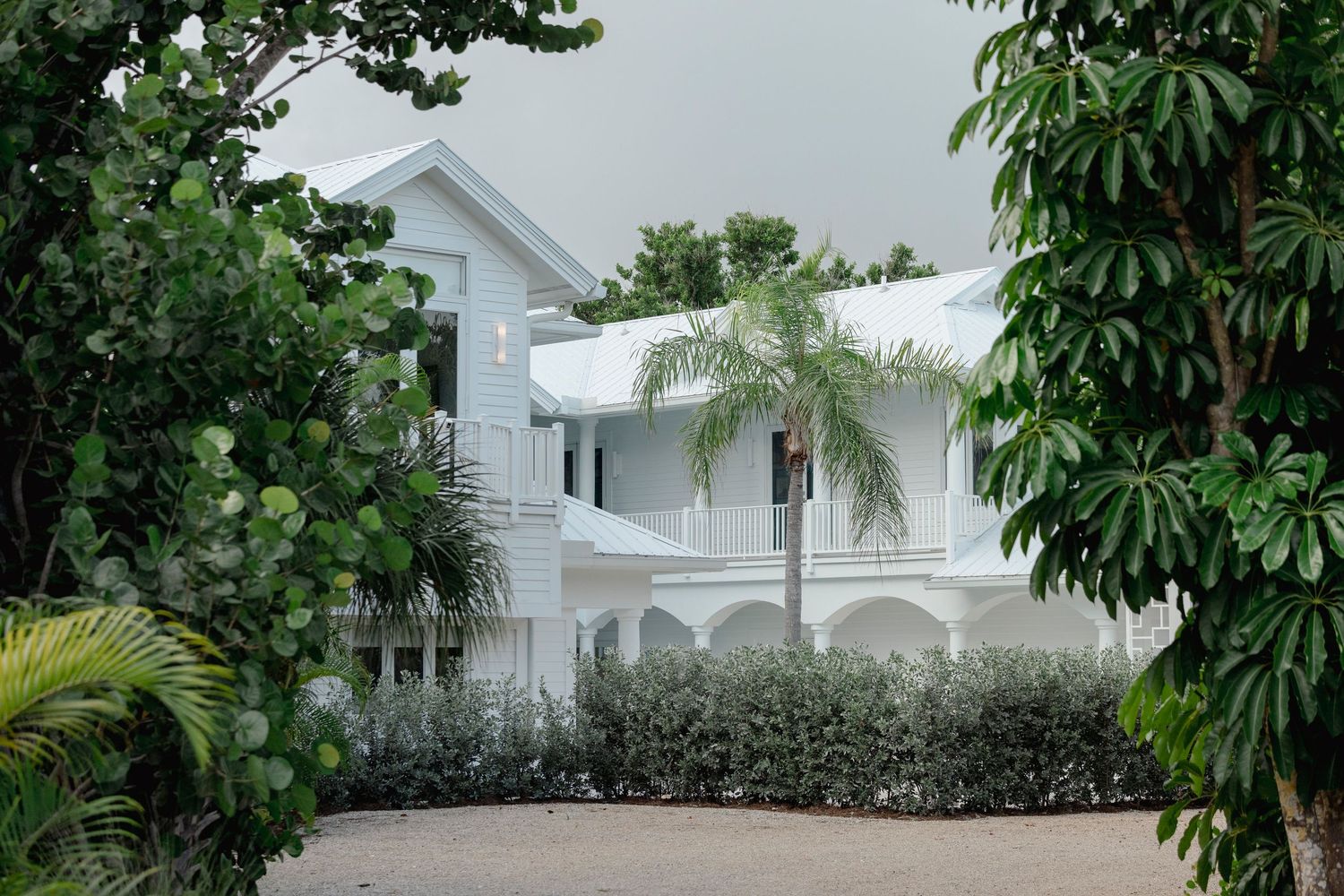 White coastal home exterior surrounded by lush tropical landscaping and palm trees.
