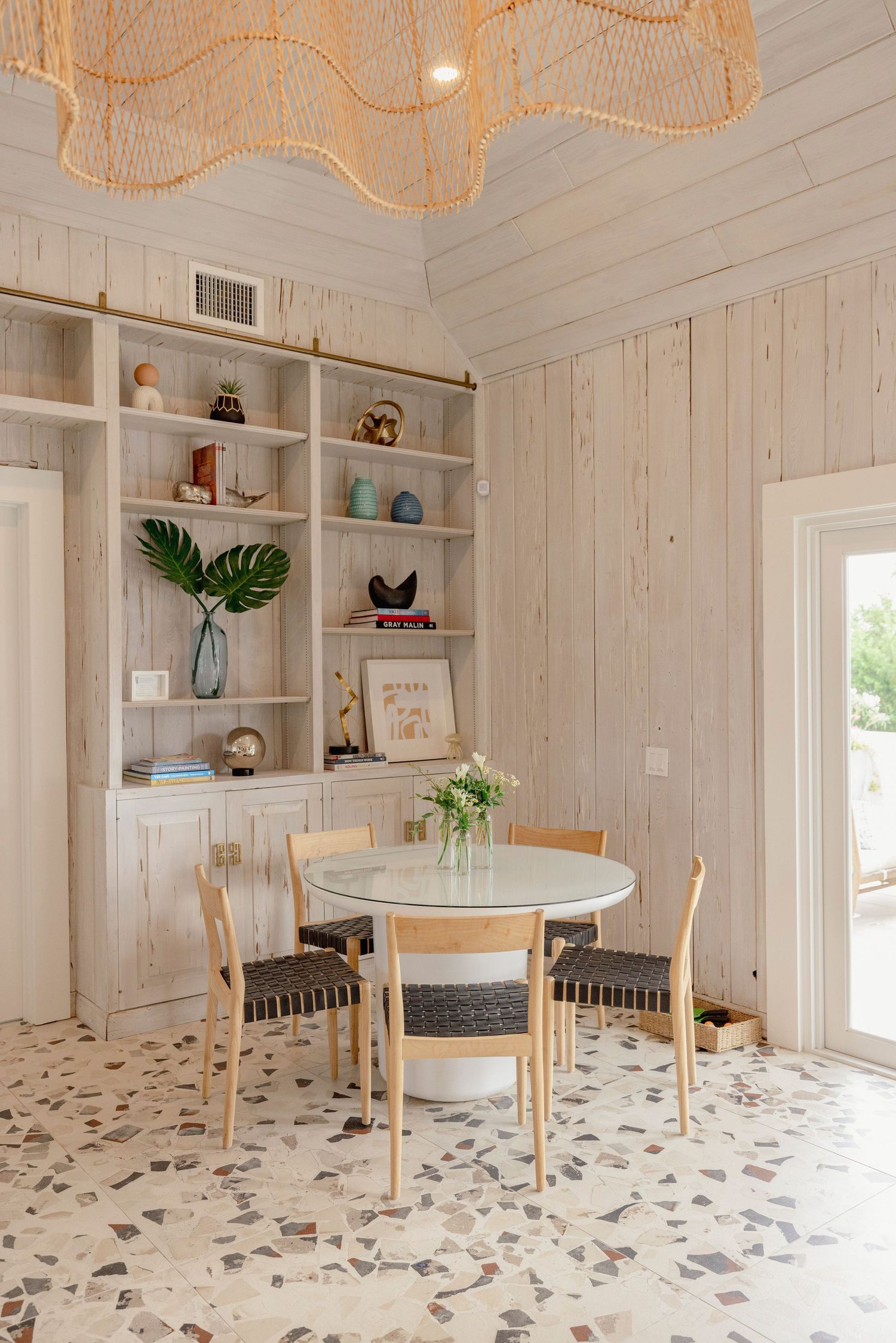White dining room with terrazzo flooring, round table, and decorative pendant lights.