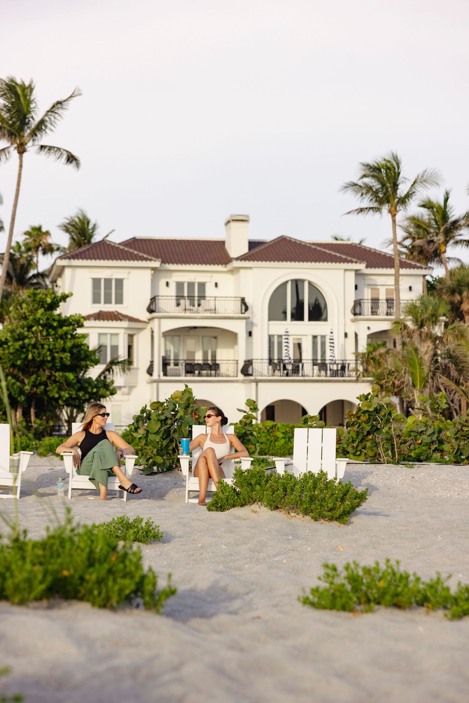 Luxury beachfront homes with Mediterranean architecture and palm trees line the sandy shoreline.