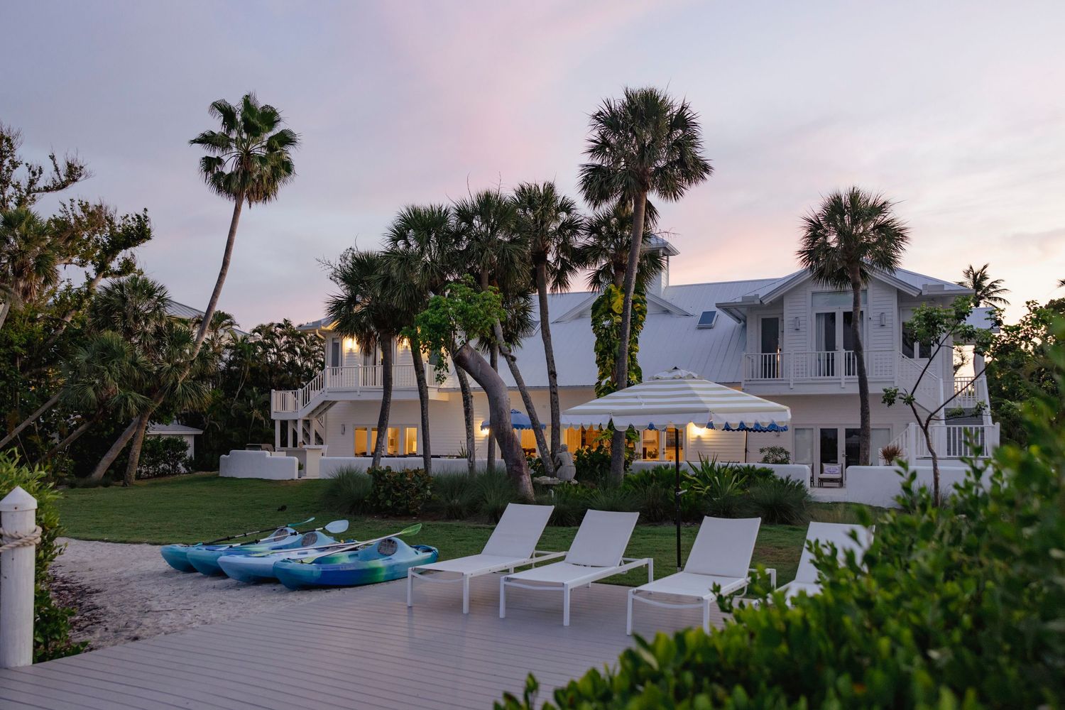 Beachfront property with palm trees and lounge chairs at sunset overlooking the ocean and sandy shore.