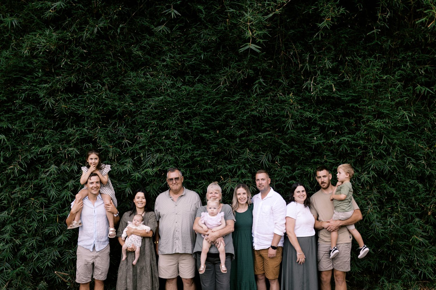 A group of people in coordinated wedding party attire standing against green foliage backdrop.