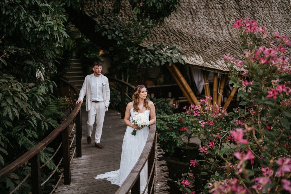 A couple strolls along a garden path with pink bougainvillea flowers blooming nearby.