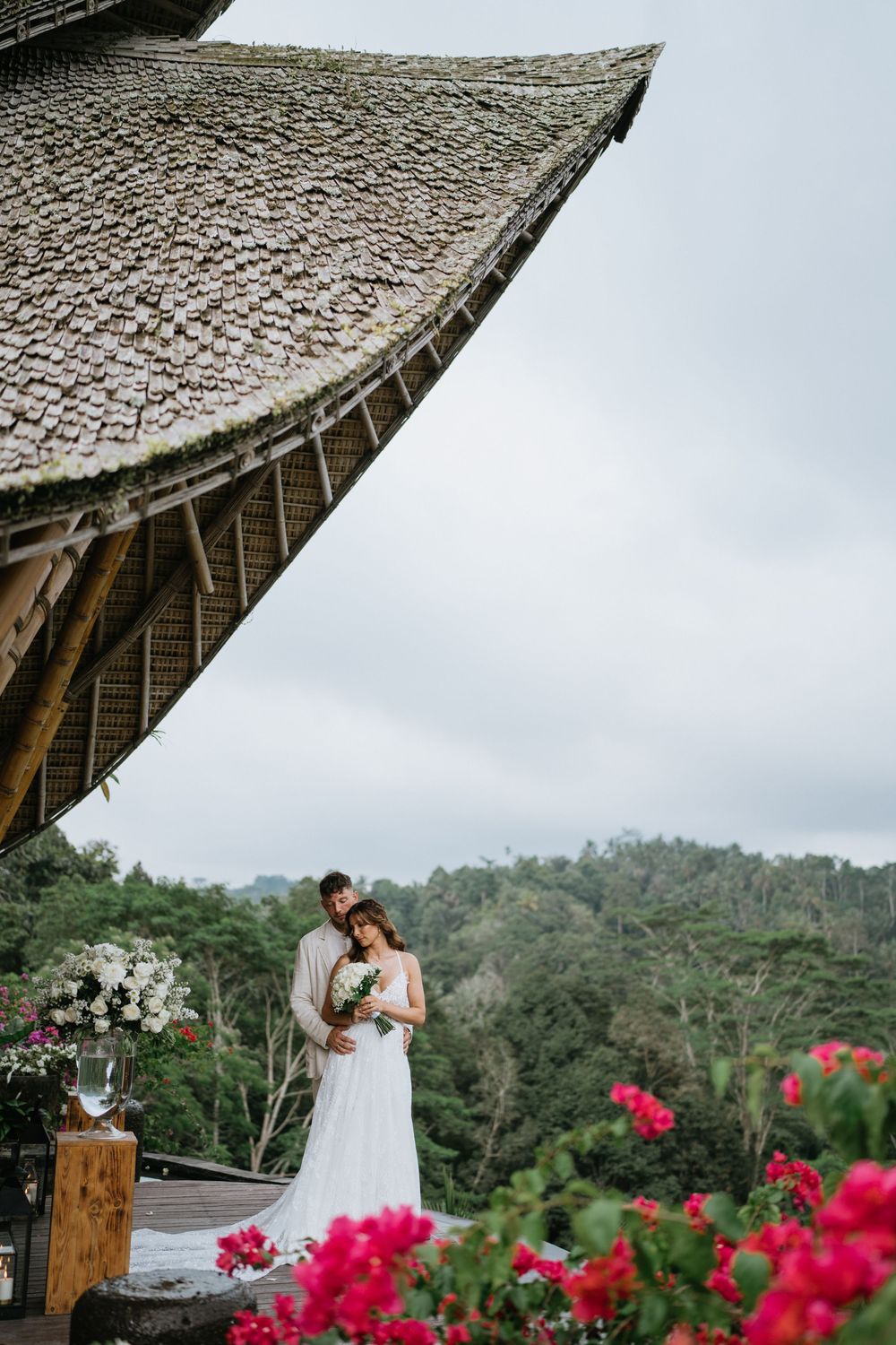 A romantic moment captured under a thatched roof pavilion with pink flowers and mountain views.