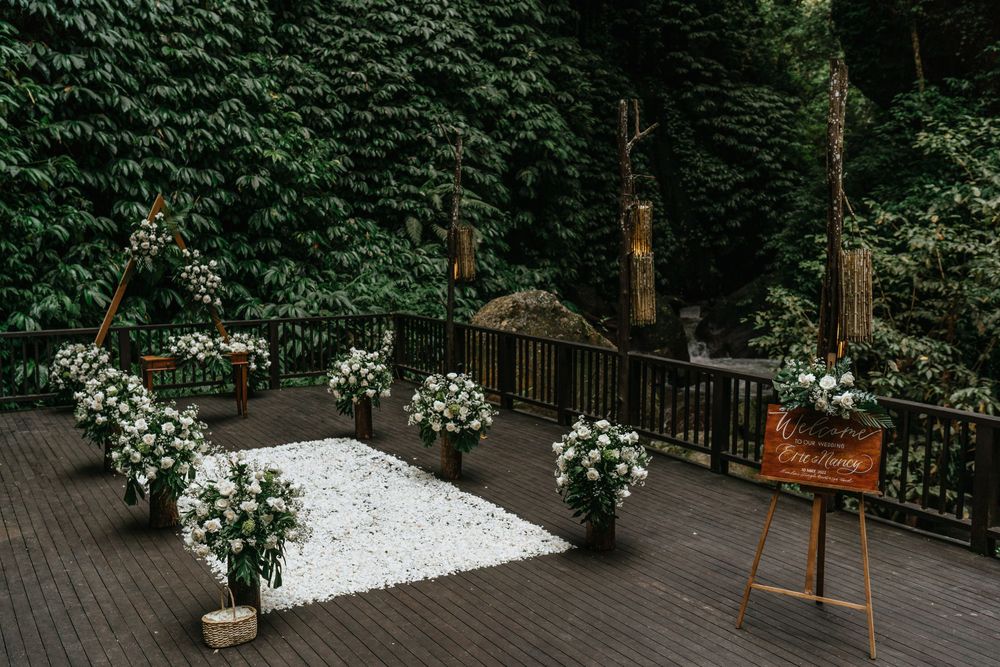 An outdoor wedding ceremony space with white floral arrangements and a white aisle runner against an ivy wall.