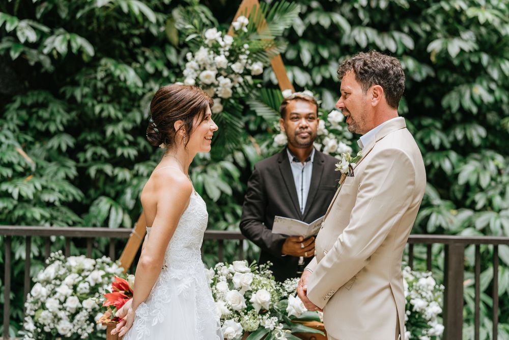 An intimate outdoor wedding ceremony takes place on a wooden deck surrounded by ivy and white flowers.
