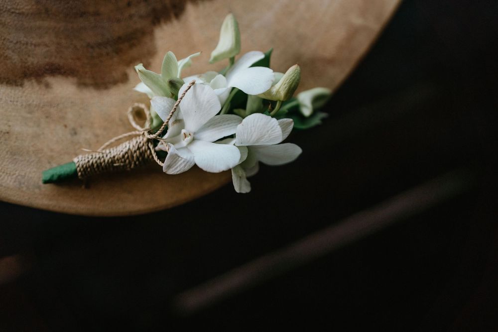 A delicate white floral boutonniere wrapped in twine rests on a dark surface.