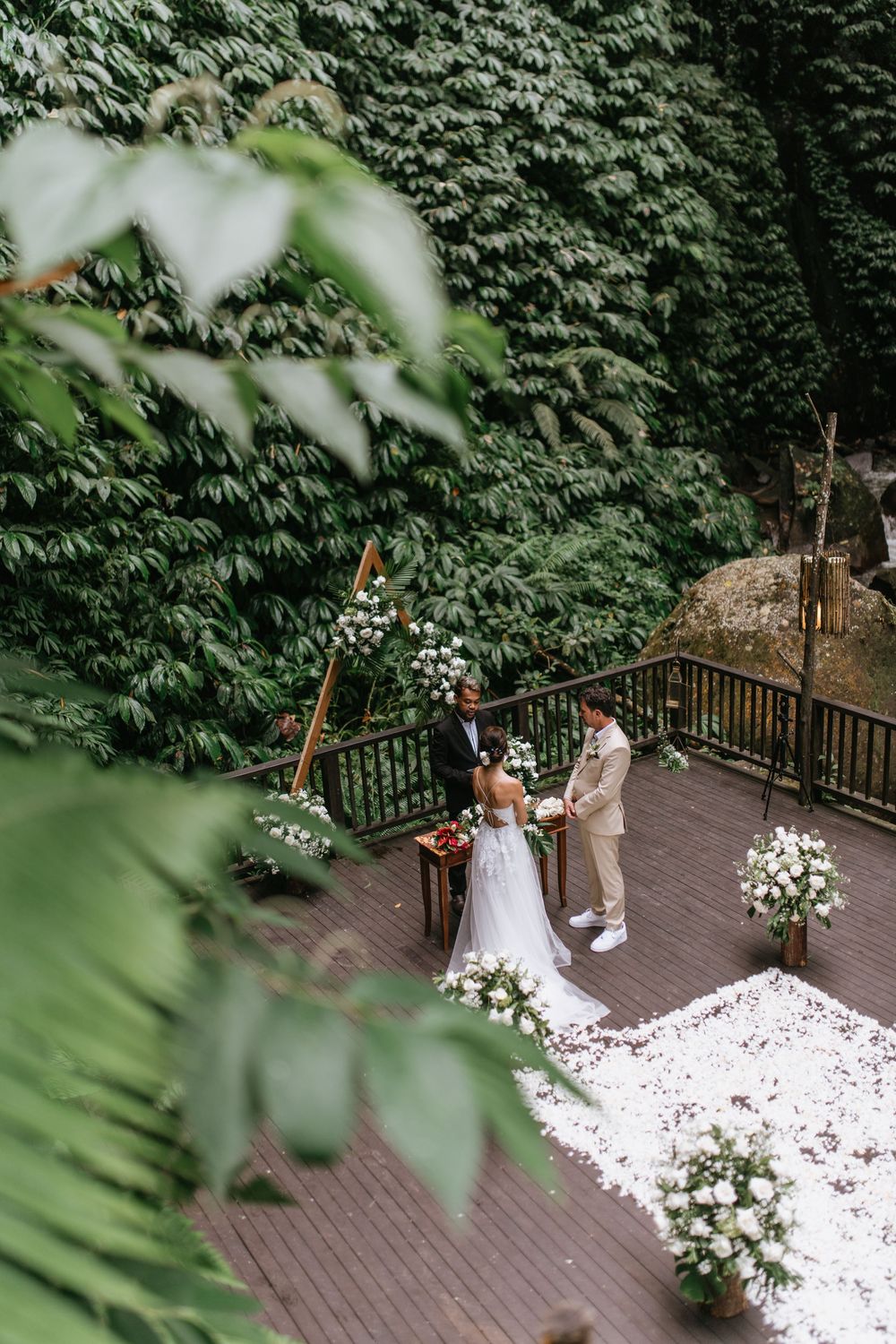 An aerial view of a wedding ceremony on a wooden deck surrounded by lush green foliage.