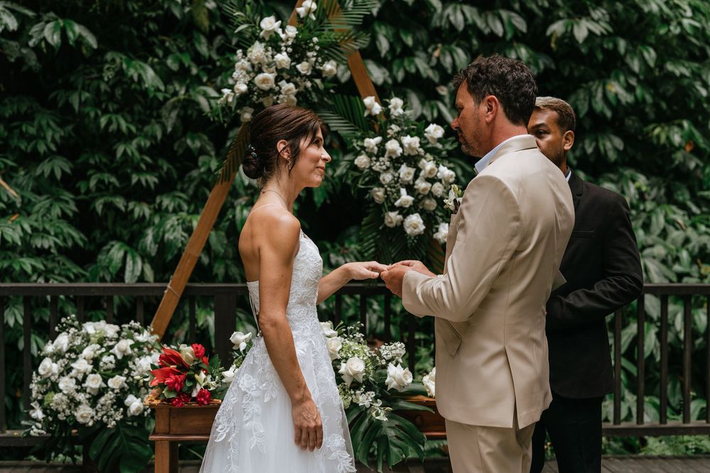 A wedding ceremony moment captured on a wooden deck with white floral decorations and green ivy backdrop.