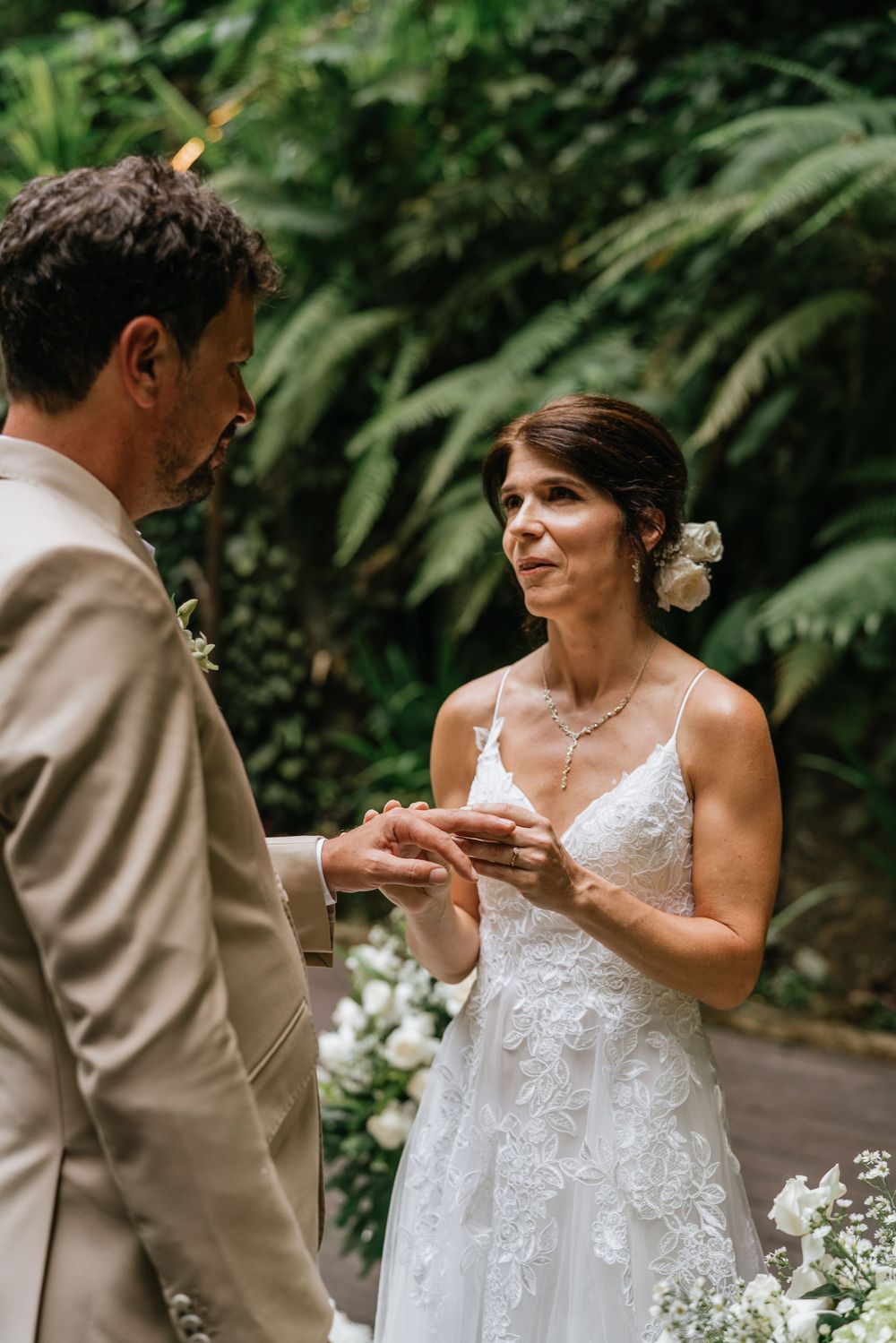 A tender moment during a wedding ceremony with white flowers and lush greenery in the background.