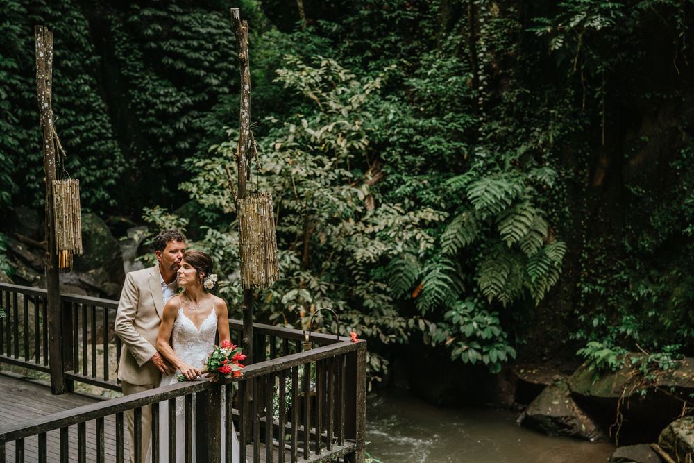 A wedding couple stands together on a wooden walkway surrounded by lush forest vegetation.
