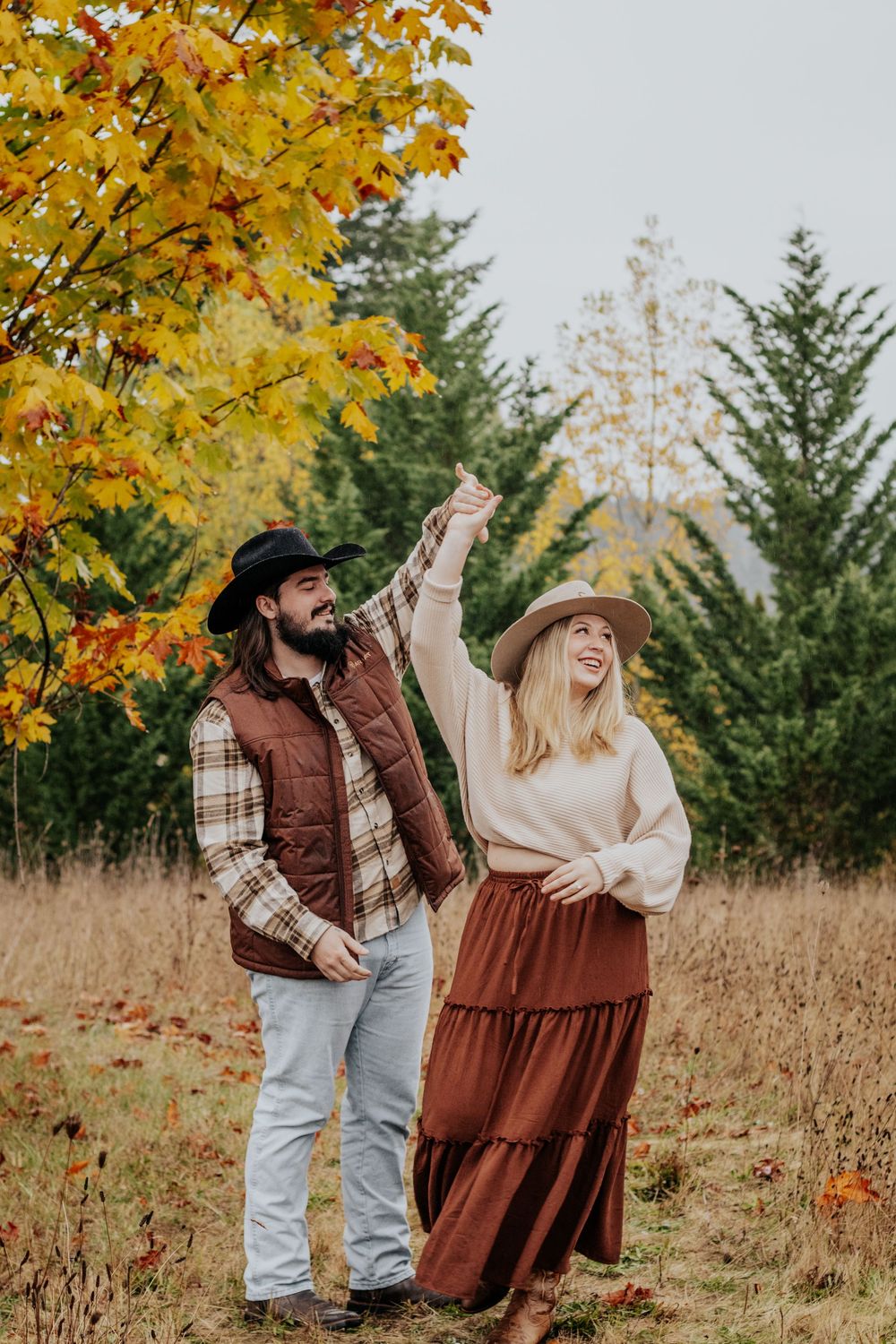 Couple dancing in fall meadow, man in cowboy hat twirling woman in brown skirt.