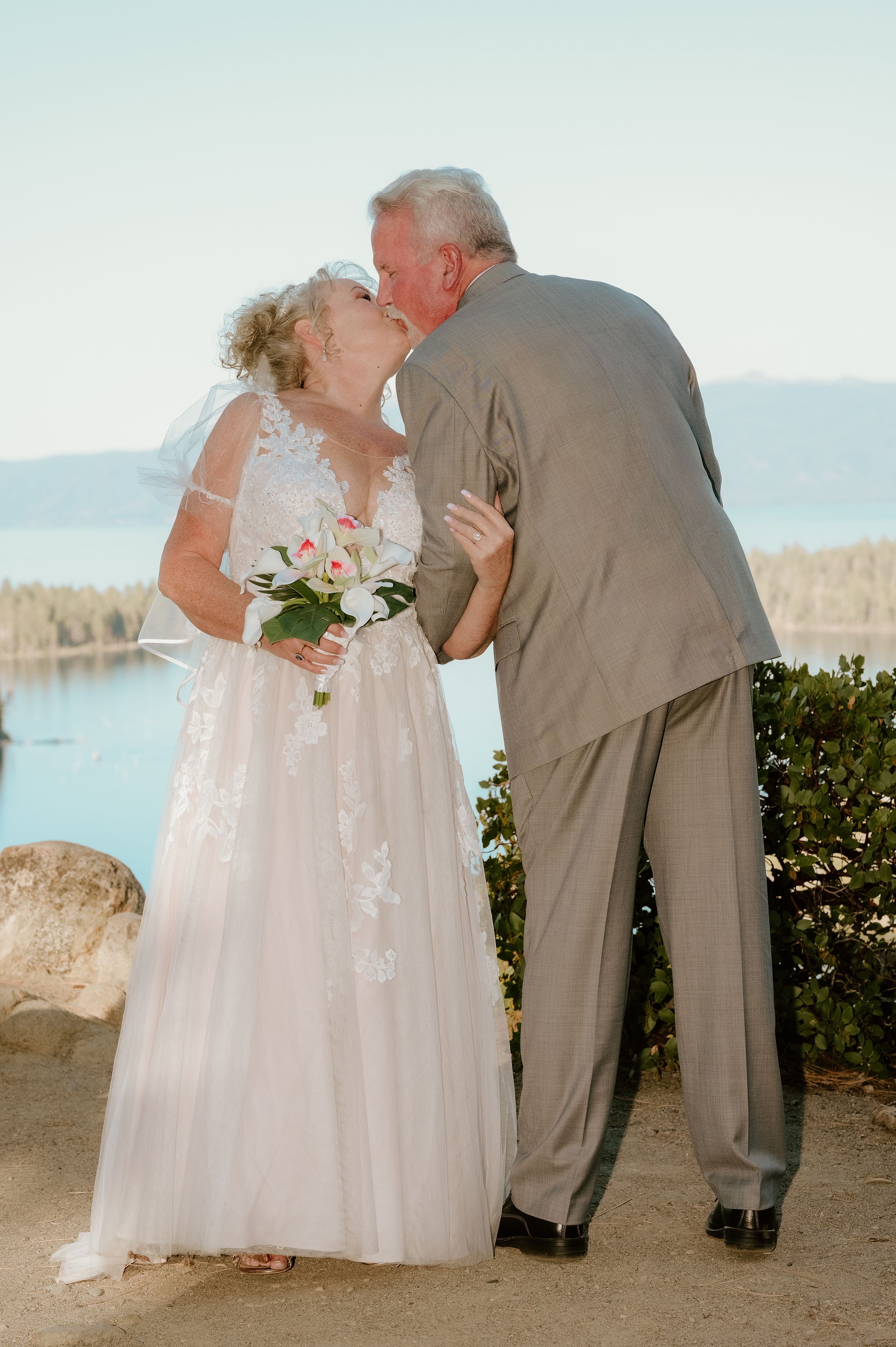 A couple shares a romantic kiss at their wedding ceremony overlooking a scenic ocean view.