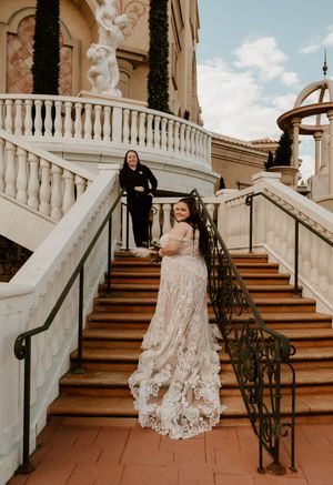 Elegant lace wedding dress train flows beautifully down grand stone staircase at outdoor venue with wrought iron railings.