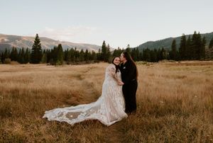 Scenic mountain vistas frame a couple in formal wear embracing in a golden autumn field during a romantic photo session.