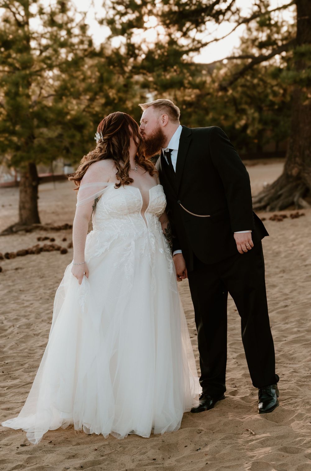 A wedding couple shares romantic moments in a series of shots on a sandy beach with pine trees in the background.