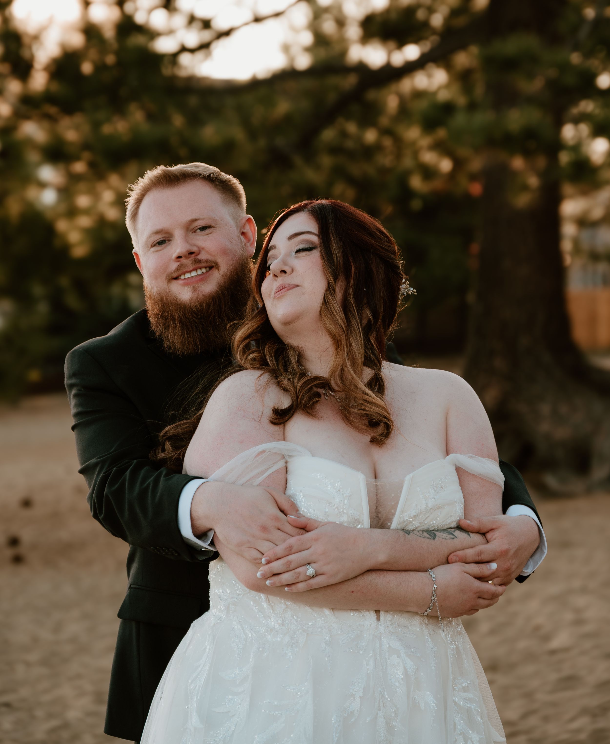 A couple embraces intimately during a golden hour photography session on sandy terrain.