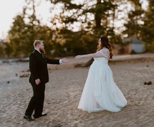 A bride and groom hold hands while spinning on a beach at sunset during their wedding celebration.