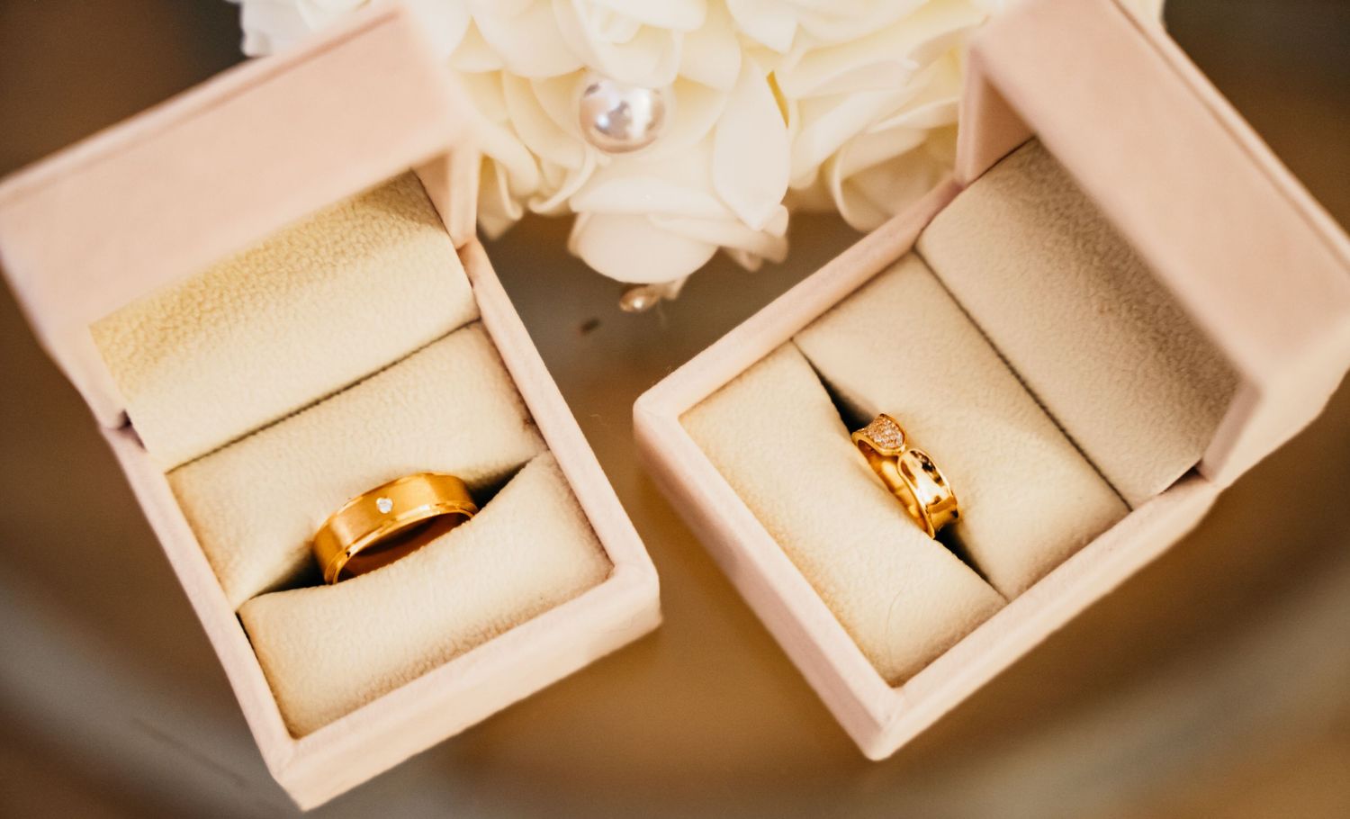 Several elegant engagement rings sit in white jewelry boxes on a warm wooden surface with soft lighting.