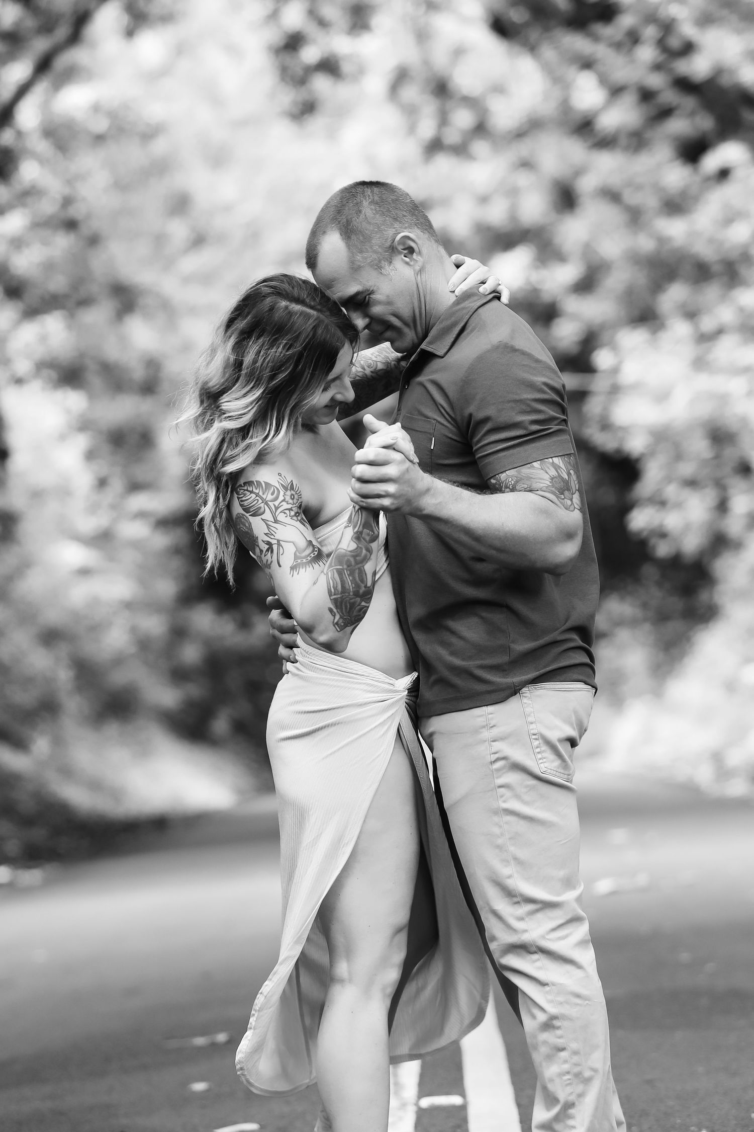A romantic black and white photo of a couple dancing intimately outdoors on a blurred nature background.