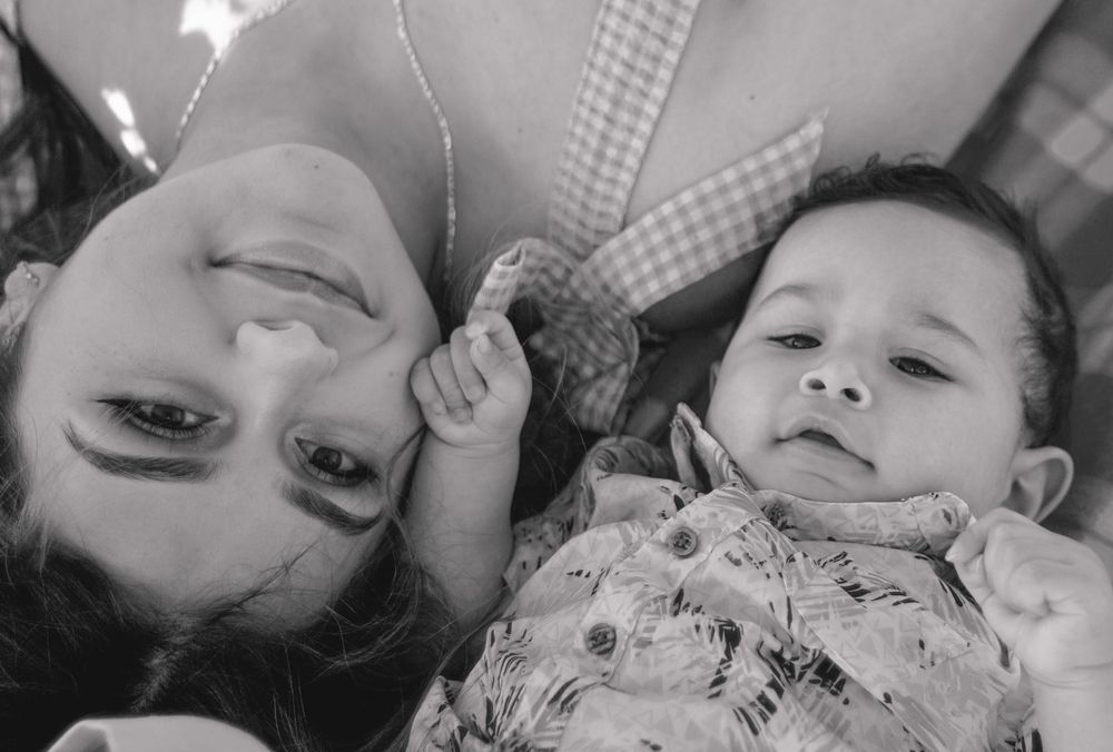 Black and white photo of a mother lying down with her smiling baby in a tender moment.