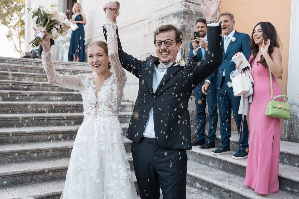 Joyful celebration on stone steps as newlyweds raise hands in victory amid confetti shower.