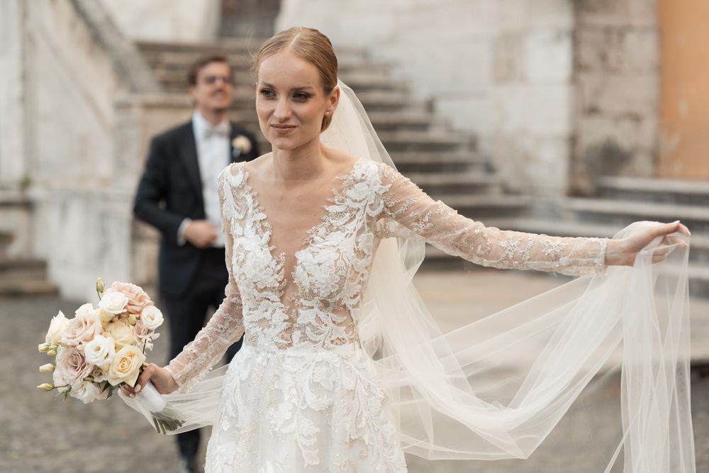 Radiant bride showcasing lace wedding dress and veil on historic stone staircase.