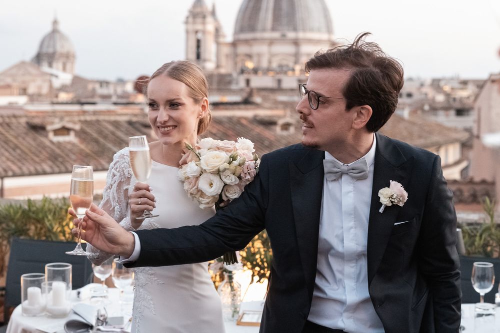 Newlyweds share a romantic moment on a rooftop terrace overlooking Rome's historic domed architecture at sunset.