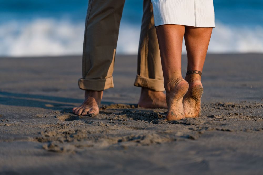Bare feet of two people standing close together in the wet sand at the beach.