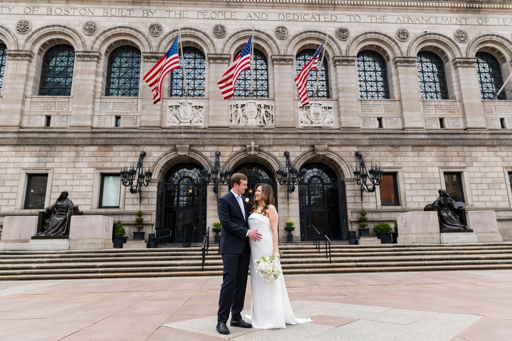 Wedding couple poses in front of Boston Public Library with American flags.