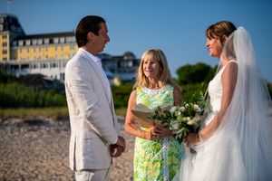 Beach wedding ceremony with officiant in floral dress at golden hour.