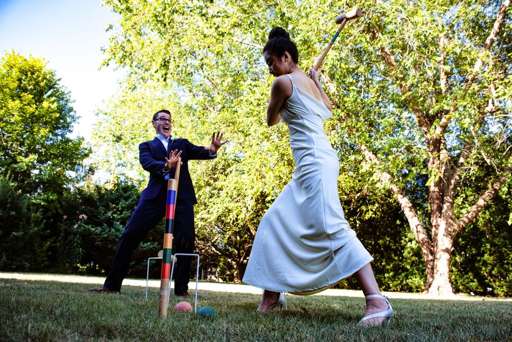Bride and groom play croquet in garden during outdoor wedding reception.