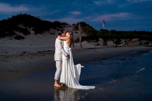 Newlyweds share romantic kiss on beach shore at twilight.
