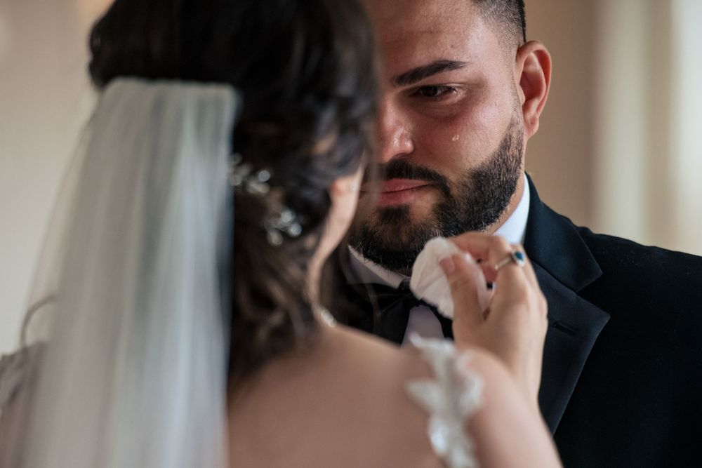 Emotional groom wiping tears during wedding ceremony as bride tenderly holds his face.