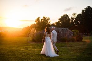 Bride and companion walking across sunlit lawn during golden hour sunset wedding celebration.