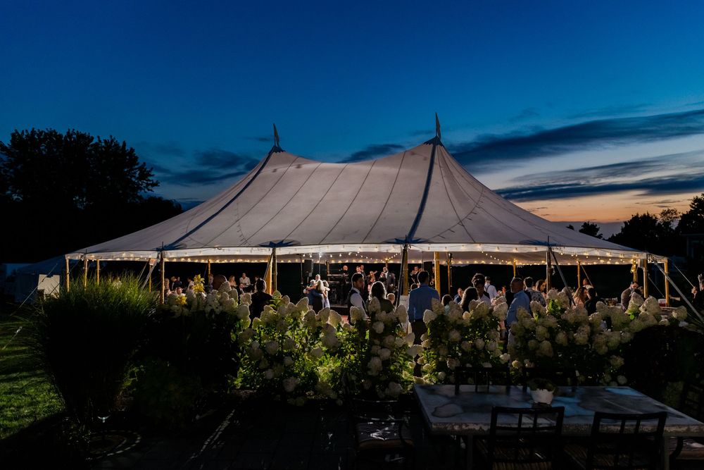 Elegant sailcloth wedding tent glowing with warm lights against a stunning twilight sky.