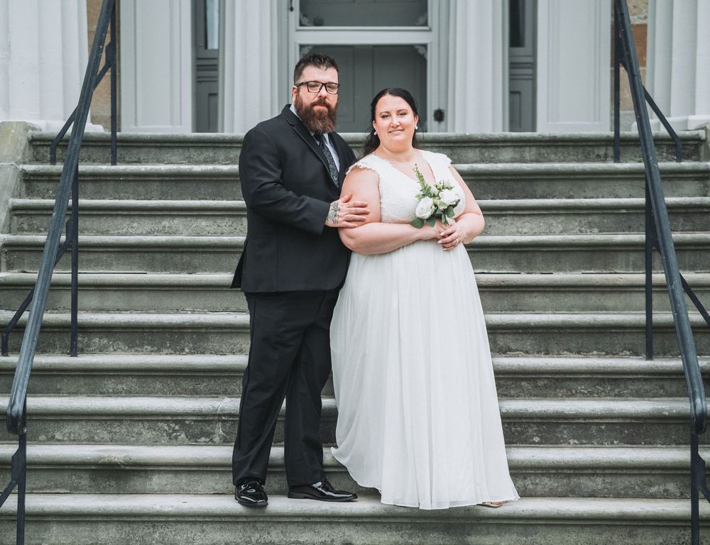 A wedding couple stands together on stone steps in front of a building entrance.