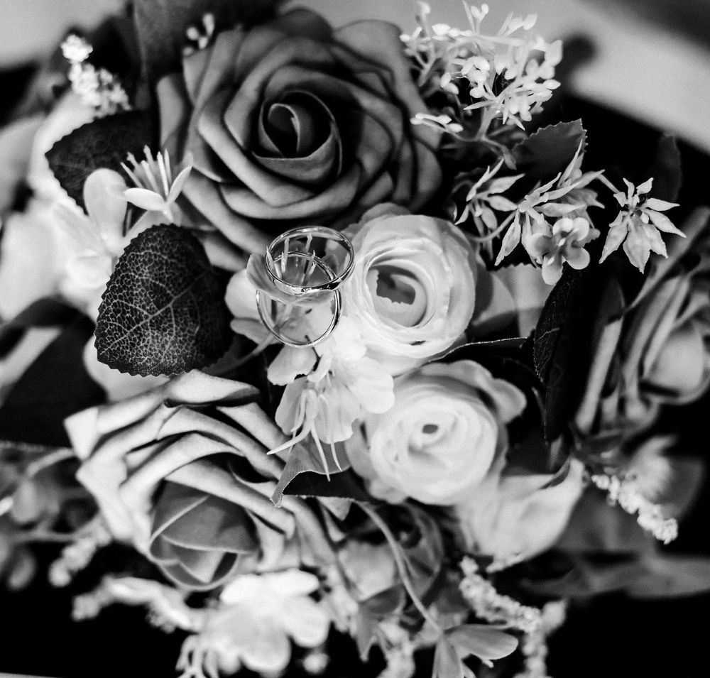 Black and white photo of a wedding bouquet with roses and a pair of rings nestled among the flowers.