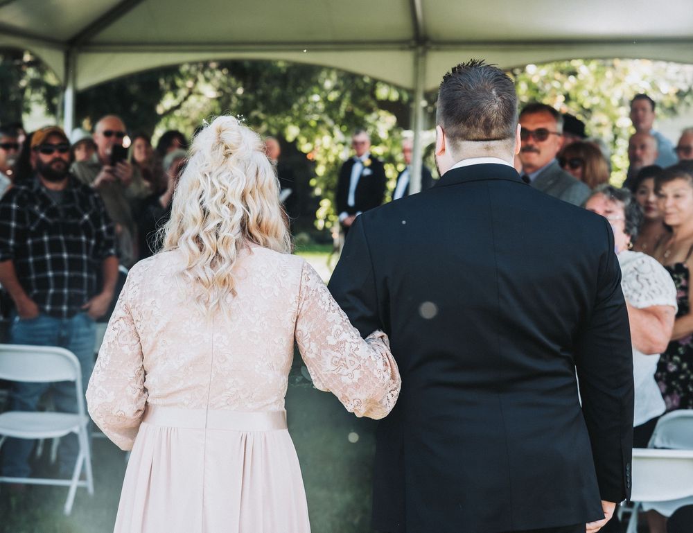 Wedding guests gather under a white tent during an outdoor reception celebration.