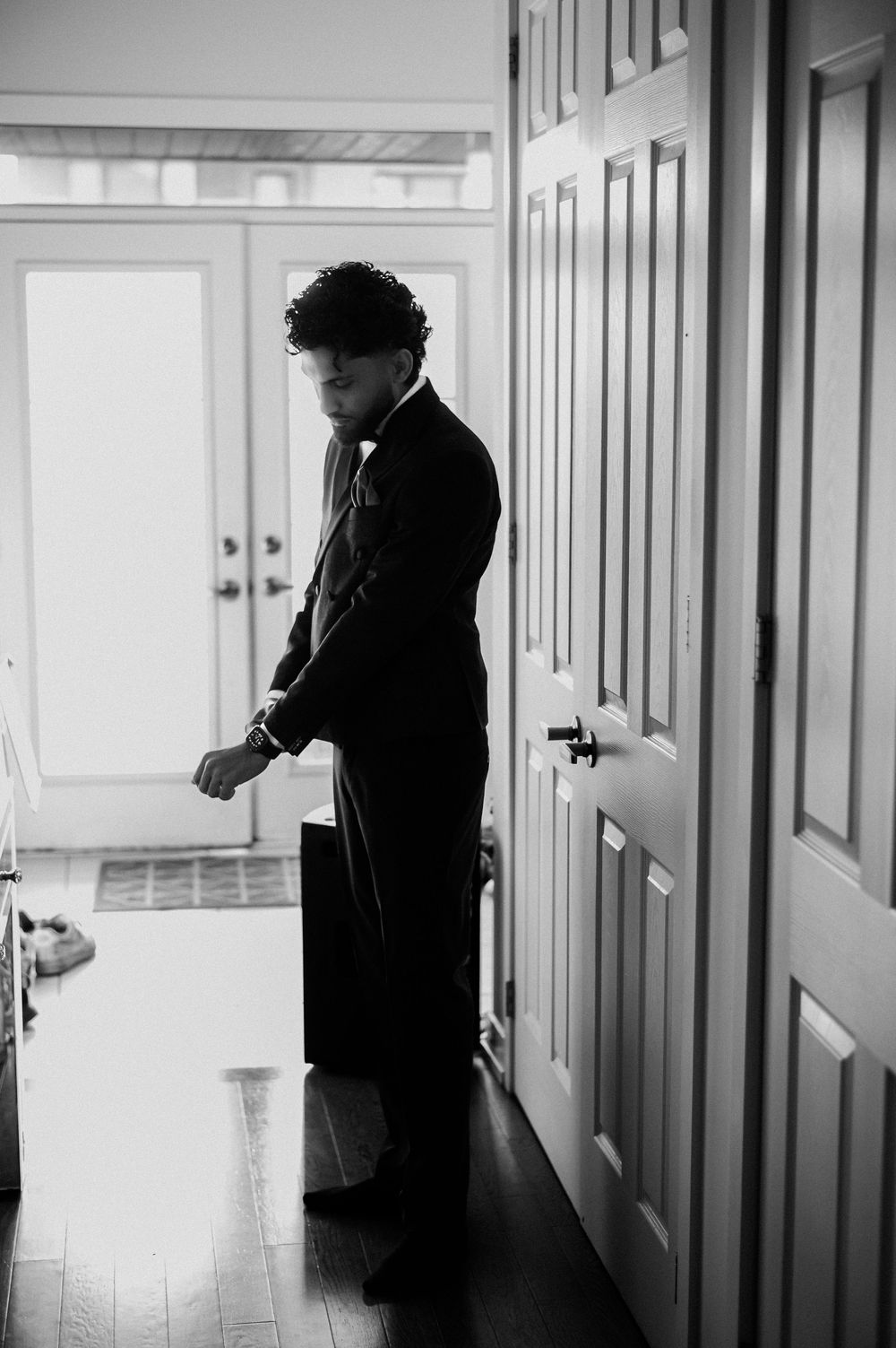 A silhouetted figure in formal wear stands in a bright hallway.