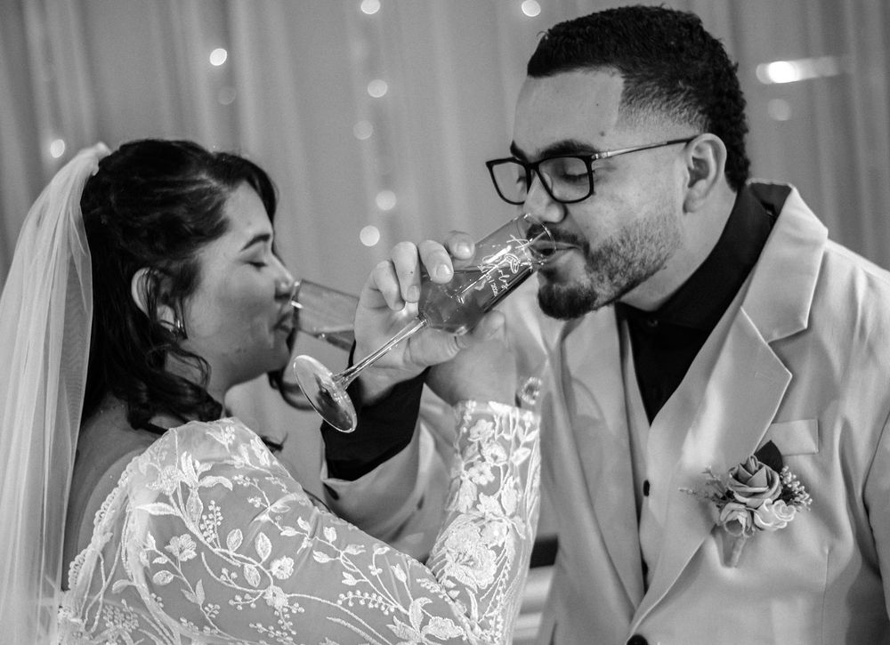 Black and white wedding photo of bride and groom sharing a drink together at their reception celebration.