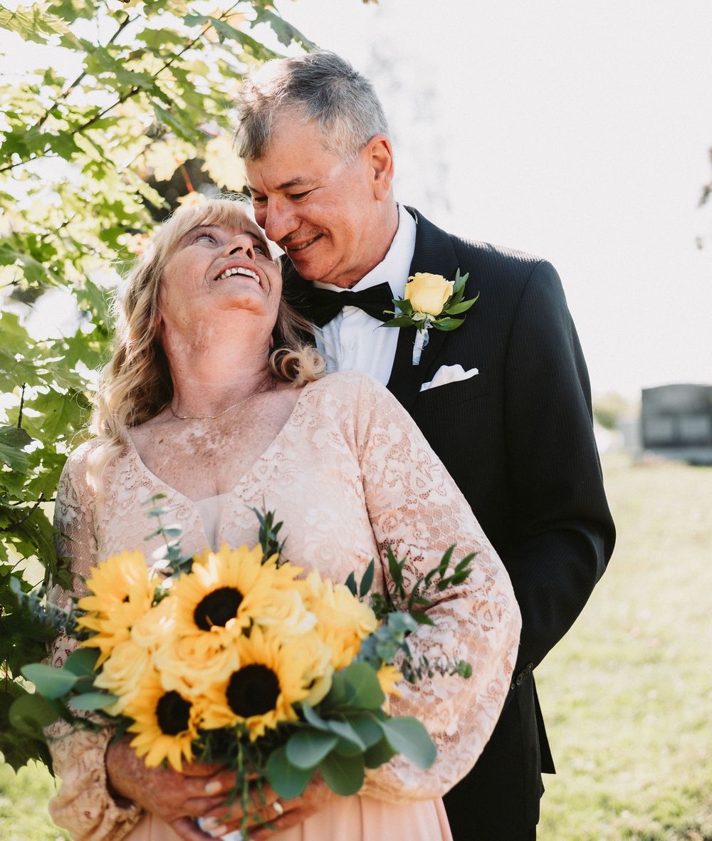 A couple embraces while holding a vibrant sunflower bouquet during an outdoor celebration.