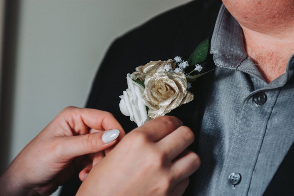 A boutonniere with white roses is being pinned onto formal wedding attire.